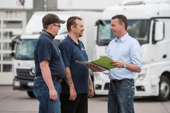 
Przedsiębiorca z branży transportowej rozmawia z dwoma kierowcami ciężarówek